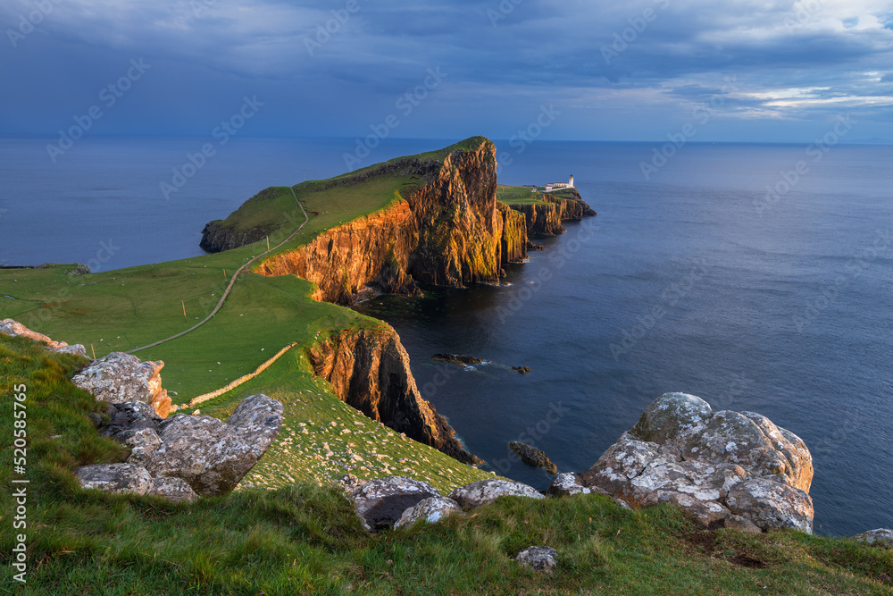 Golden evening sunlight casting on cliffs of Neist Point Lighthouse on the Isle of Skye, Scotland, UK.