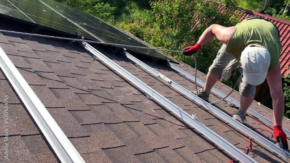 Worker carefully steps on roof installing new generation effective solar panels. DIY PV panels assembly on bituminous tiles roof Worker carefully steps on roof installing new generation effective solar panels. DIY PV panels assembly on bituminous tiles roof