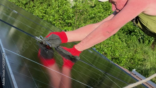 Worker fasten bolt installed solar PV panels roof of small house. Reflection from solar panel on hot day