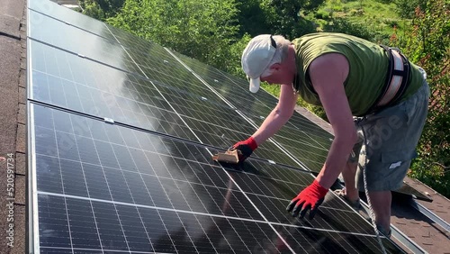 Man fastens bolt installing solar panels on tiles roof of small house. Green energy generation of PV panels high efficiency
