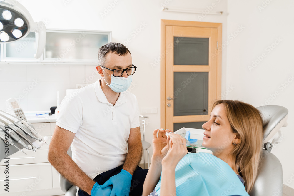 Orthodontist shows mouth guard for teeth whitening in dentistry. Dentist consult woman patient about home teeth whitening procedure. Orthodontist shows mouth guard for teeth whitening in dentistry. Dentist consult woman patient about home teeth whitening procedure.