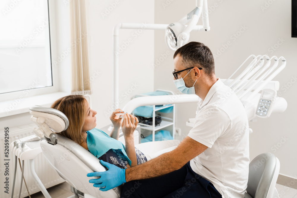 Dentist consult woman about using removable clear braces aligner, orthodontic silicone trainer. Portrait girl with white smile using invisible whitening tray. Smiling woman with healthy teeth. Dentist consult woman about using removable clear braces aligner, orthodontic silicone trainer. Portrait girl with white smile using invisible whitening tray. Smiling woman with healthy teeth.