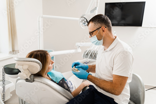 Dental prosthetics consultation with dentist for patient woman in dentistry. Doctor dentist shows artificial plastic jaw with dental implants.