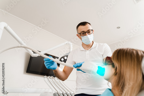 UV teeth whitening for woman patient in protective glasses in dentistry. Laser bleaching teeth in clinic. Dentist do ultraviolet whitening of teeth.