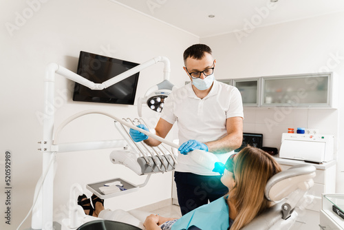 UV teeth whitening for woman patient in protective glasses in dentistry. Laser bleaching teeth in clinic. Dentist do ultraviolet whitening of teeth.