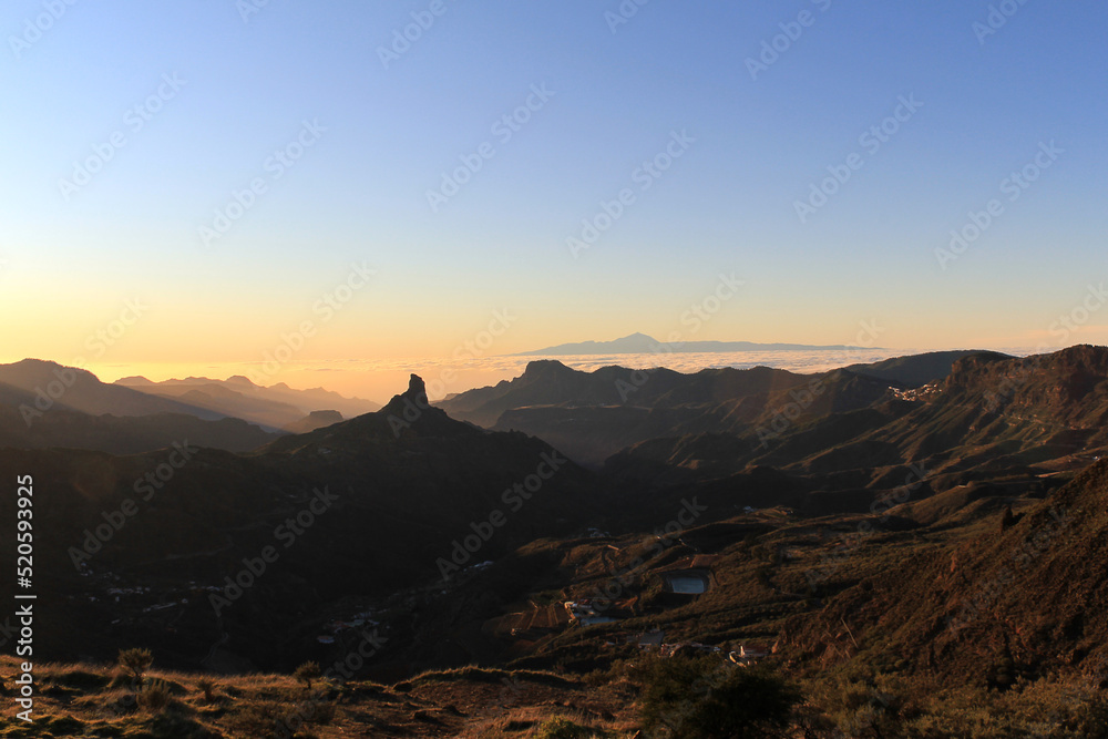 View of Roque Nublo on Gran Canaria with the silhouete of the Teide mountain in the background and a sea cloud. Sunset in Gran Canaria.