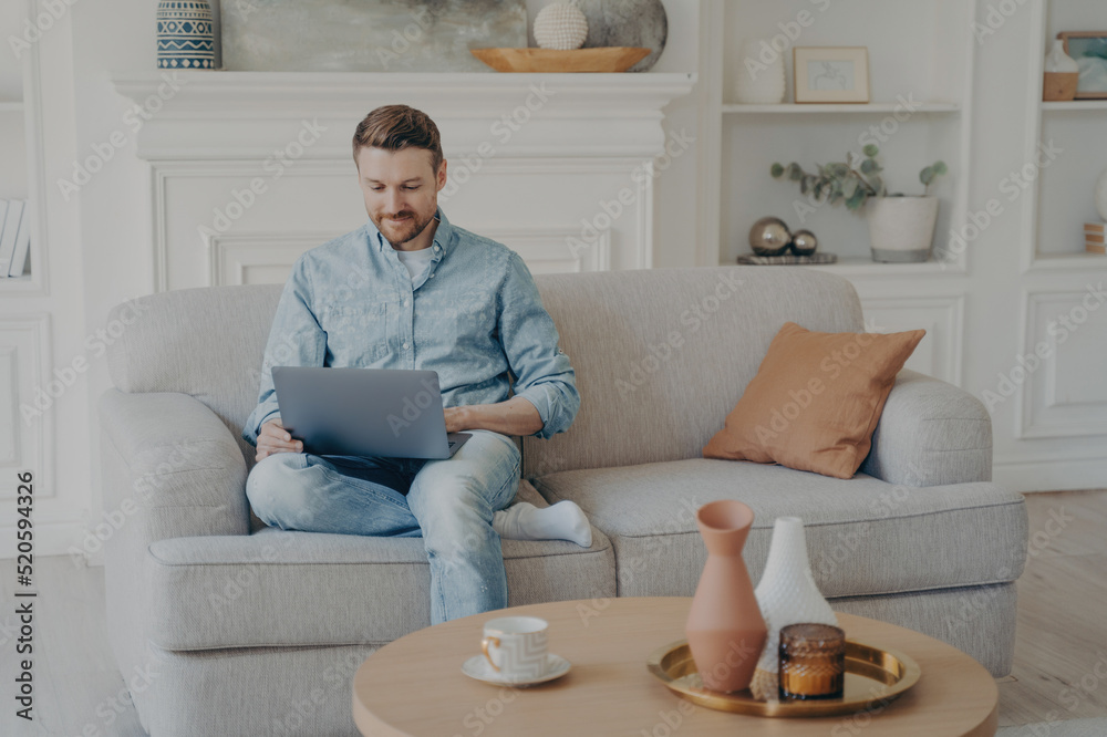 Young office worker working from home while sitting on couch with crossed leg