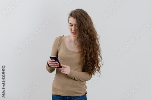 A girl with a mobile phone. Dark curly long hair. Smiling