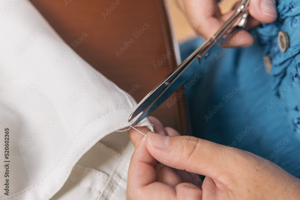 Close up shot of an unrecognizable woman's hand working with scissors to cut a thread and fix her linen pants. Seamstress at home doing tailoring work. Close up shot of an unrecognizable woman's hand working with scissors to cut a thread and fix her linen pants. Seamstress at home doing tailoring work.