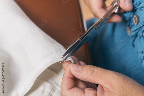 Close up shot of an unrecognizable woman's hand working with scissors to cut a thread and fix her linen pants. Seamstress at home doing tailoring work.