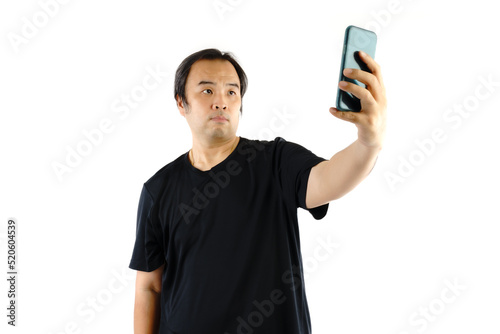 Asian man wear black t-shirts. Using mobile To take a picture  or selfie of himself isolated on white background. © Vatcharachai