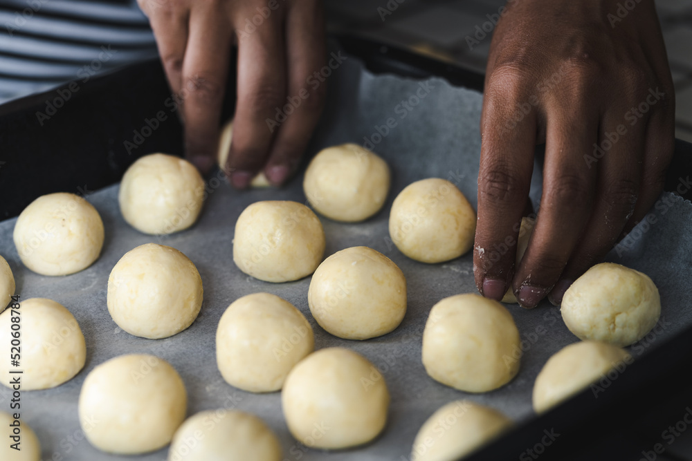 Latin woman placing rolls of chipa in the baking pan, traditional small cheese-flavored rolls