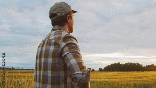 Farmer in front of a sunset agricultural landscape. Man in a countryside field. Country life, food production, farming and country lifestyle.