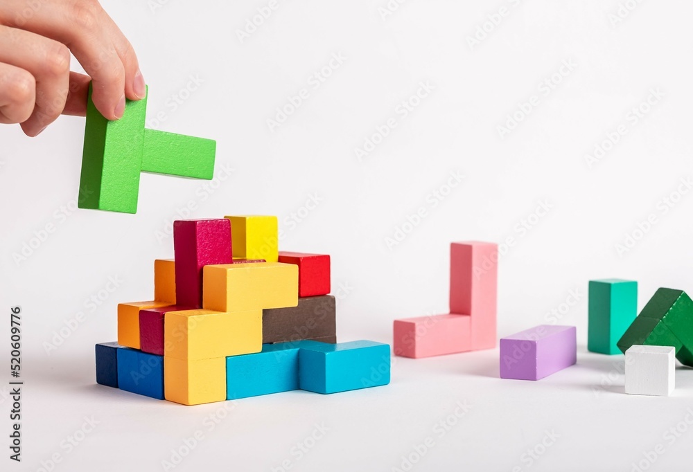Hand assembling tetris puzzle, searching appropriate place for wooden block. Construction, formation concept. Finding solution to problem. Logical thinking, reasoning strategy development. photo Hand assembling tetris puzzle, searching appropriate place for wooden block. Construction, formation concept. Finding solution to problem. Logical thinking, reasoning strategy development. photo
