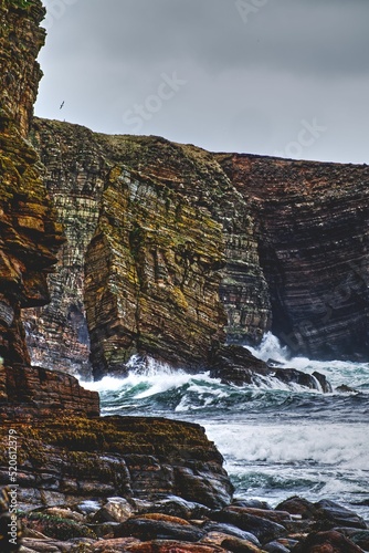 Seascape view with white foamy waves and high rocky cliffs in Ossi Taing, Orkney, Scotland photo