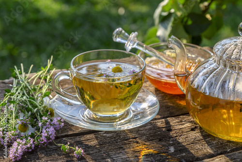 Herbal tea with chamomile and thyme in a transparent cup on an old wooden table on a sunny day