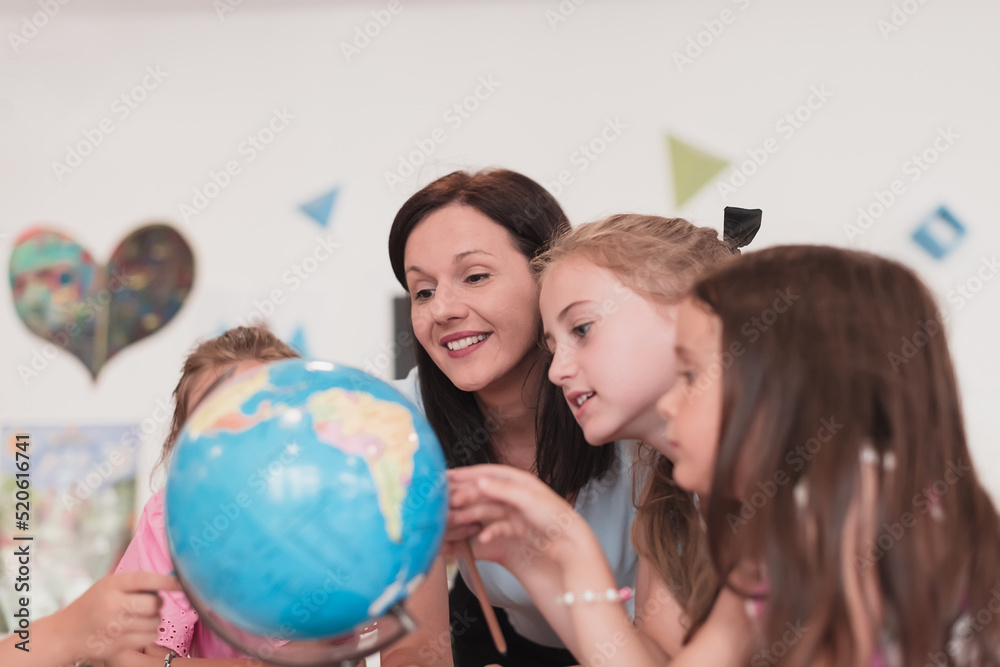 Female teacher with kids in geography class looking at globe. Side view of group of diverse happy school kids with globe in classroom at school. Female teacher with kids in geography class looking at globe. Side view of group of diverse happy school kids with globe in classroom at school.