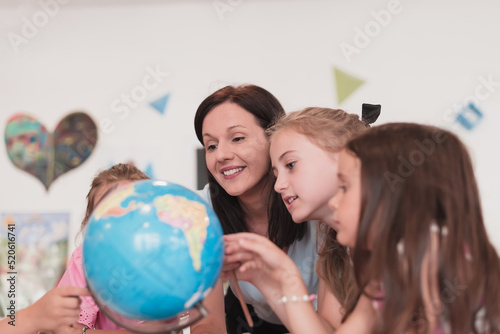 Female teacher with kids in geography class looking at globe. Side view of group of diverse happy school kids with globe in classroom at school.