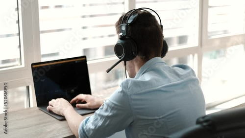 Young businessman wear headset video conference calling on laptop computer talk by webcam in online chat, customer support service and distance online teaching concept
