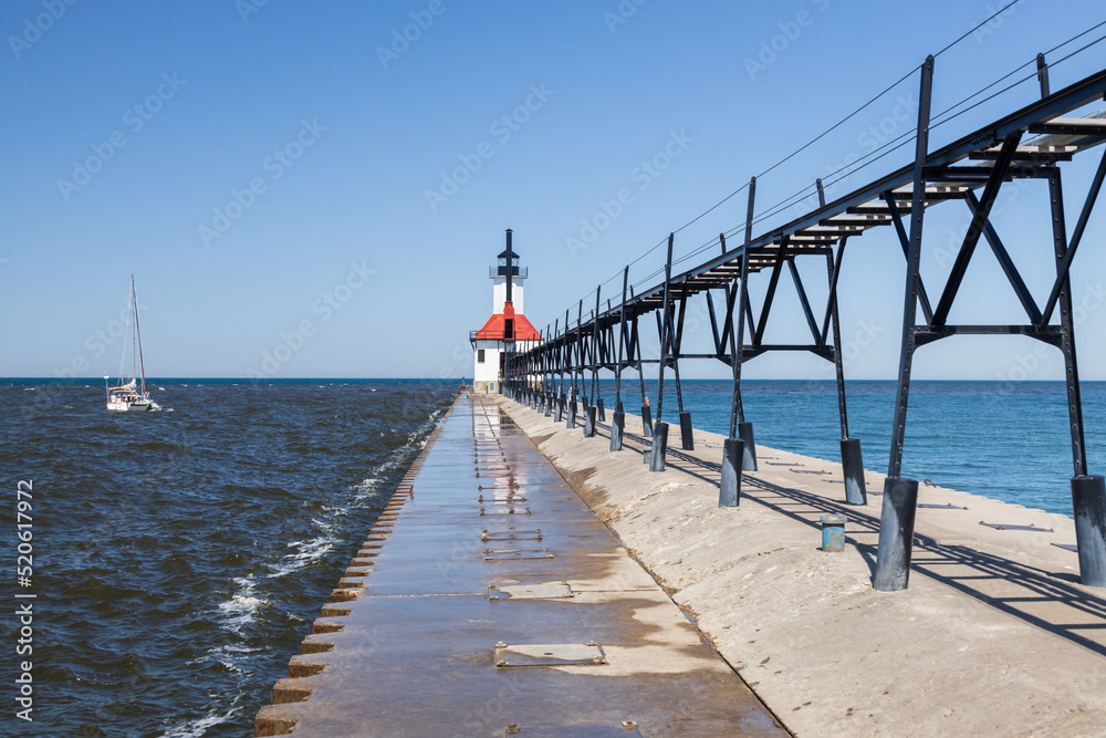 Obraz premium Sailboat going out the channel at St. Joseph North Pier Lighthouse, Michigan