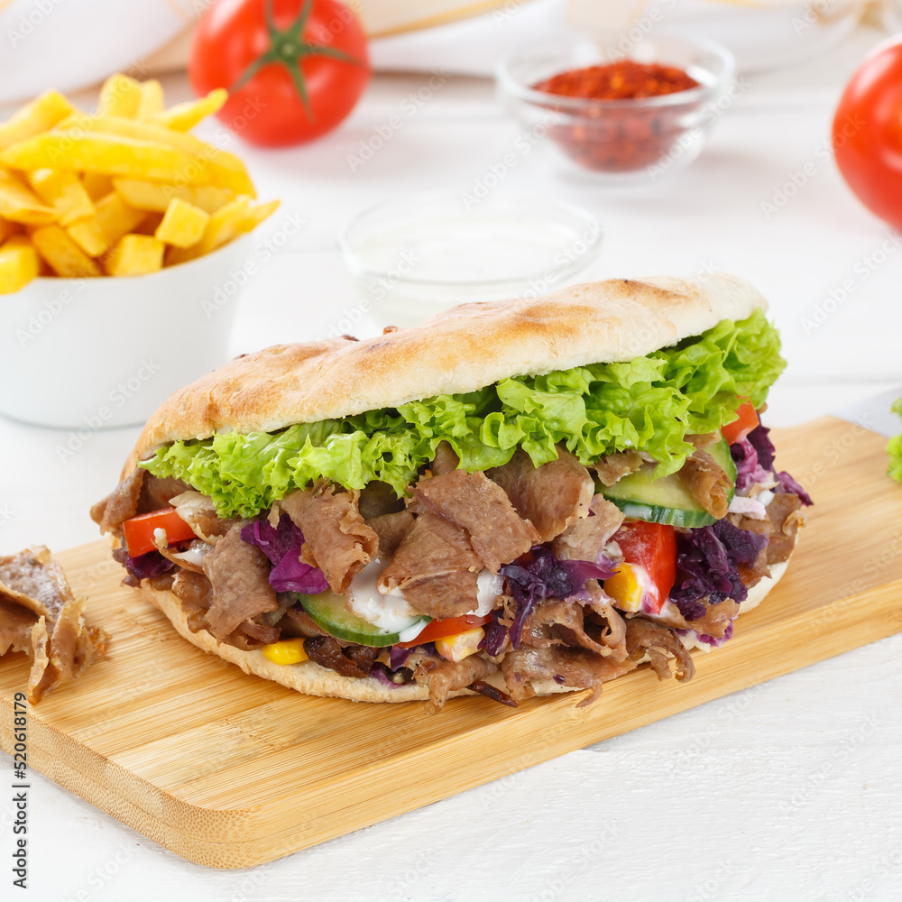 Döner Kebab Doner Kebap fast food meal in flatbread with fries on a kitchen board square Döner Kebab Doner Kebap fast food meal in flatbread with fries on a kitchen board square
