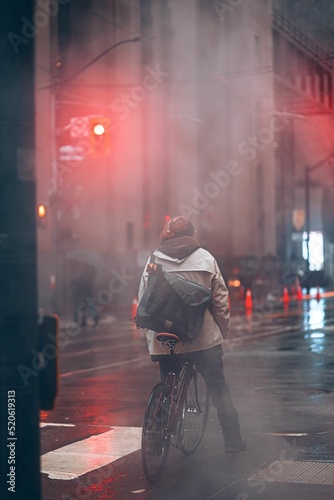 Photography Vertical back view of a male riding a bike in the street on a rainy day in Toron