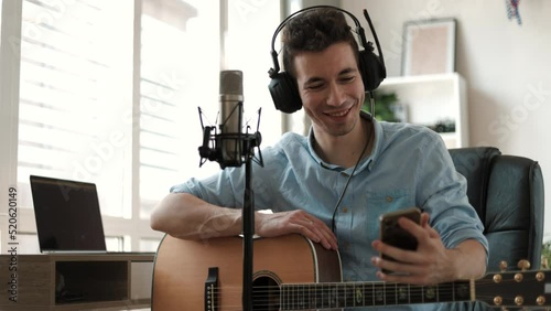 Male guitar player sit indoor with smart phone, take break resting from playing string instrument using cellphone smiles read pleasant message. Hobby, pastime, modern wireless technology user concept
