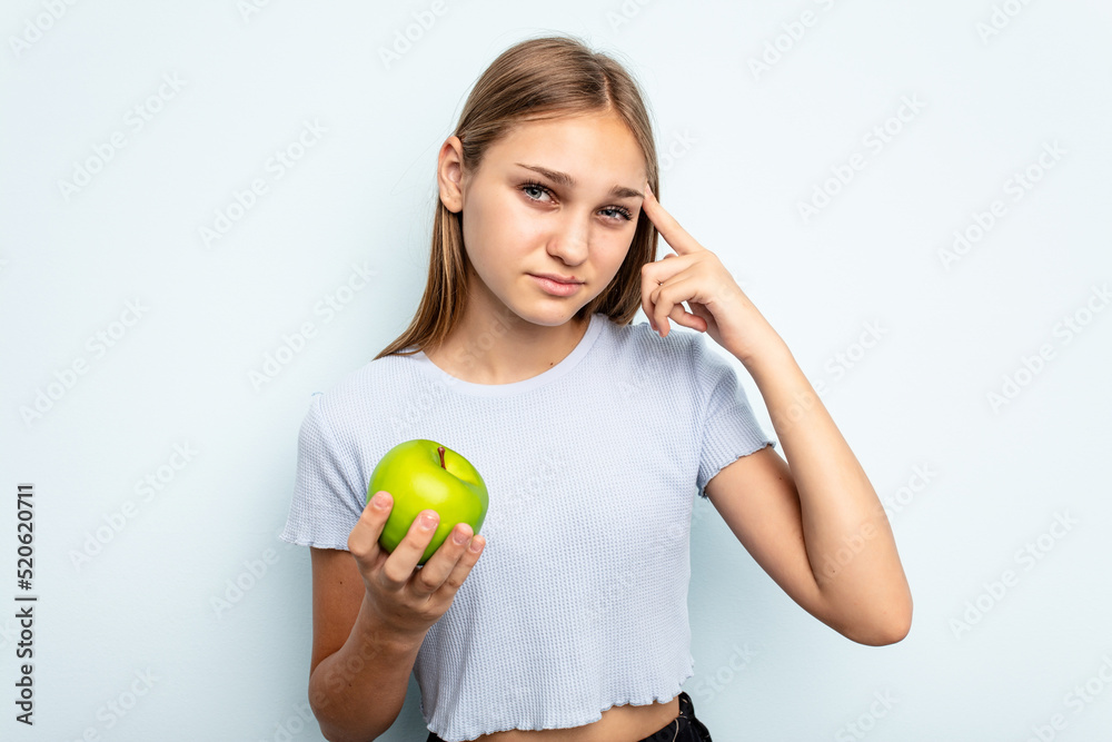 Young caucasian girl holding an apple isolated on blue background showing a disappointment gesture with forefinger. Young caucasian girl holding an apple isolated on blue background showing a disappointment gesture with forefinger.