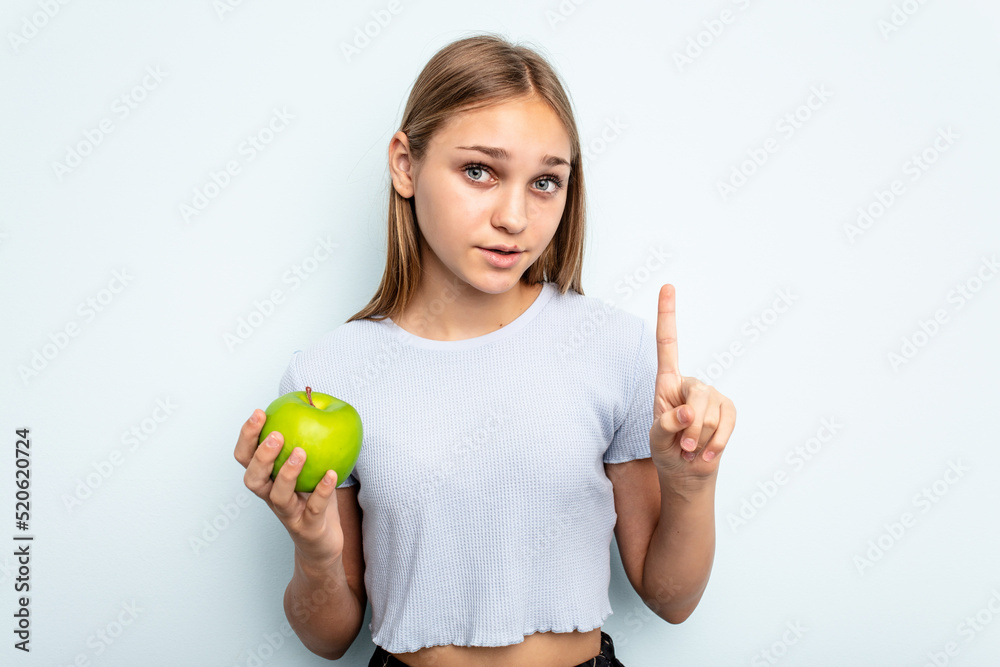 Young caucasian girl holding an apple isolated on blue background having some great idea, concept of creativity. Young caucasian girl holding an apple isolated on blue background having some great idea, concept of creativity.