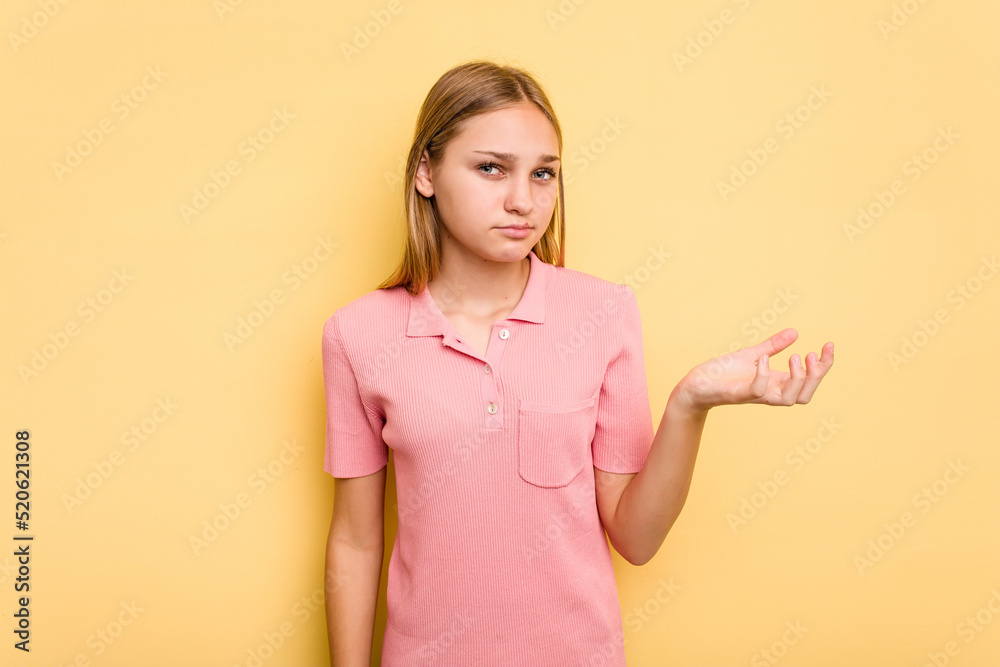 Young caucasian girl isolated on yellow background doubting and shrugging shoulders in questioning gesture. Young caucasian girl isolated on yellow background doubting and shrugging shoulders in questioning gesture.