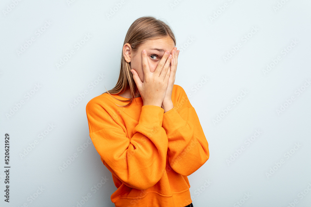 Young caucasian girl isolated on blue background blink through fingers frightened and nervous. Young caucasian girl isolated on blue background blink through fingers frightened and nervous.