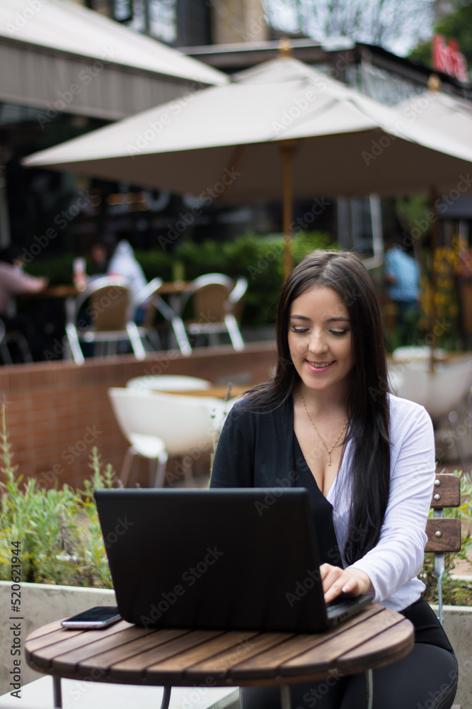 Young woman working outdoor, using a laptop computer in a cafe. Young woman working outdoor, using a laptop computer in a cafe.