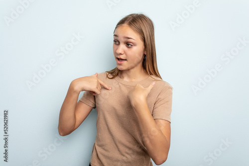 Young caucasian girl isolated on blue background surprised pointing with finger, smiling broadly.