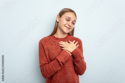 Young caucasian girl isolated on blue background laughing keeping hands on heart, concept of happiness.