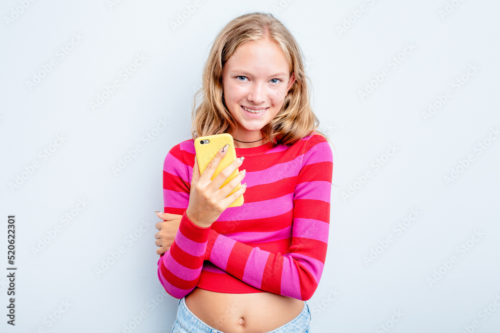 Caucasian teen girl holding mobile phone isolated on blue background laughing and having fun. Caucasian teen girl holding mobile phone isolated on blue background laughing and having fun.