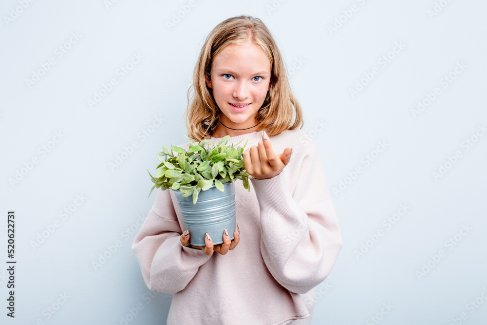 Caucasian teen girl holding a plant isolated on blue background pointing with finger at you as if inviting come closer. Caucasian teen girl holding a plant isolated on blue background pointing with finger at you as if inviting come closer.