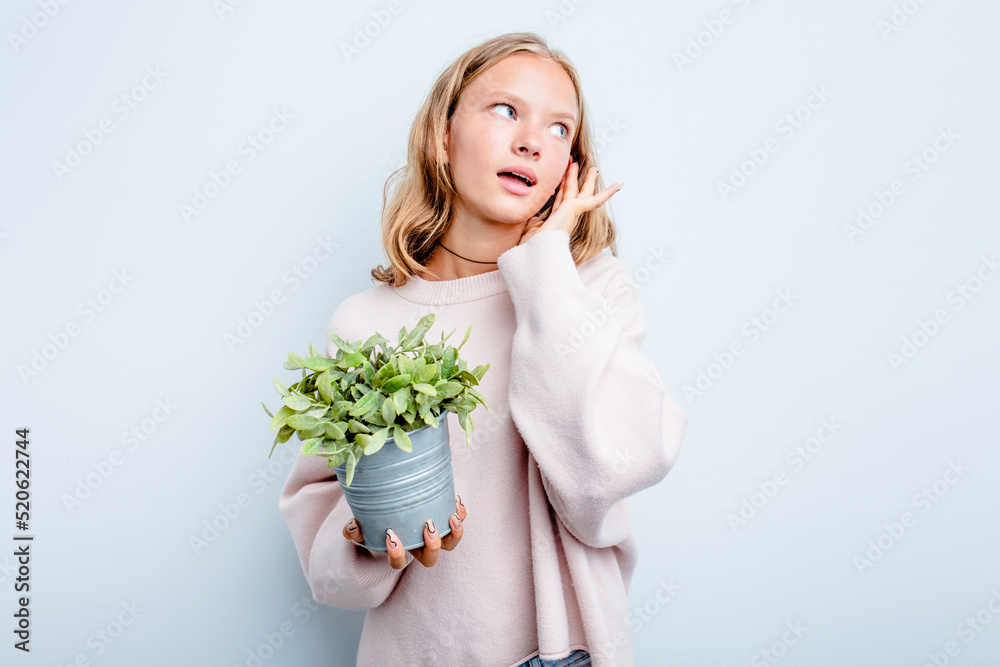 Caucasian teen girl holding a plant isolated on blue background trying to listening a gossip.