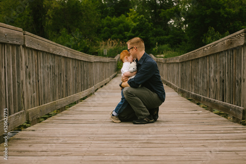 Father comforts and hugs son on a bridge in forest
