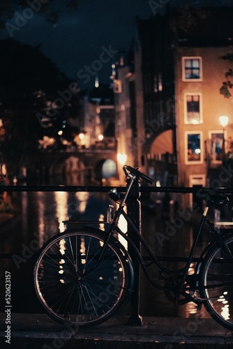Fotografiet Vertical of a bicycle parked at a handrail of a bridge at night in Amsterdam, th