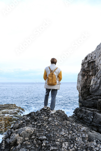Retired tourist woman standing on black rocks and looking to the sea photo