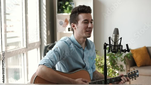 Happy Caucasian male enjoy singing by playing Guitar while sitting on sofa at home - Concept of Learning, practicing Guitar as hobby and Relaxing