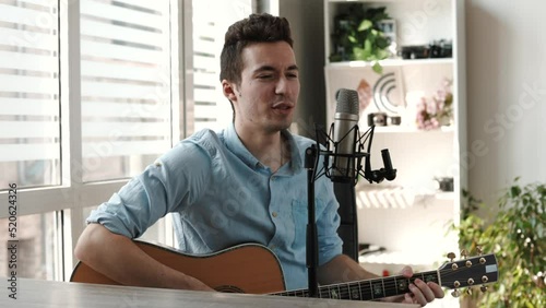 Happy Caucasian male enjoy singing by playing Guitar while sitting on sofa at home - Concept of Learning, practicing Guitar as hobby and Relaxing