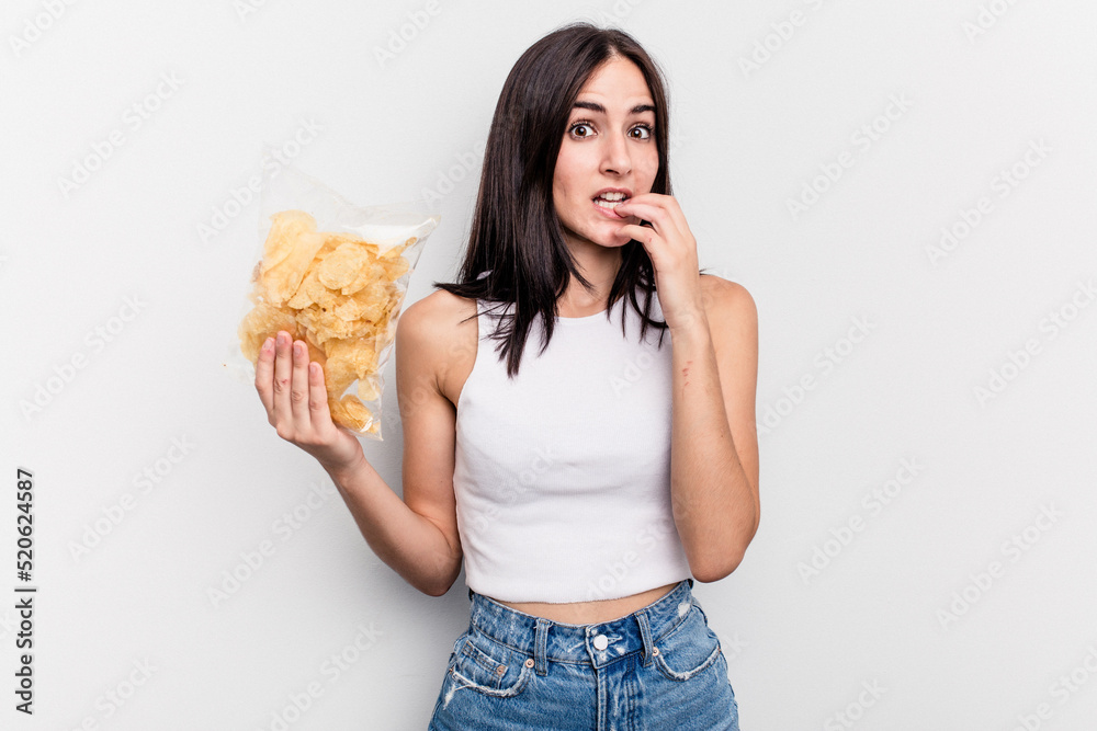 Young caucasian woman holding a bag of chips isolated on white background biting fingernails, nervous and very anxious. Young caucasian woman holding a bag of chips isolated on white background biting fingernails, nervous and very anxious.