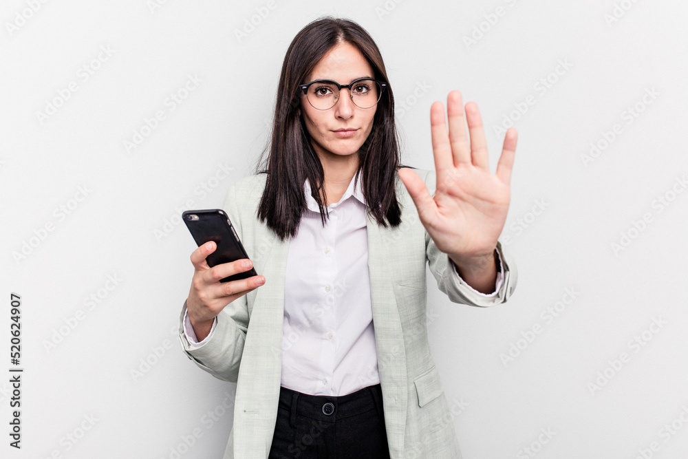 Young business caucasian woman holding mobile phone isolated on white background standing with outstretched hand showing stop sign, preventing you. Young business caucasian woman holding mobile phone isolated on white background standing with outstretched hand showing stop sign, preventing you.