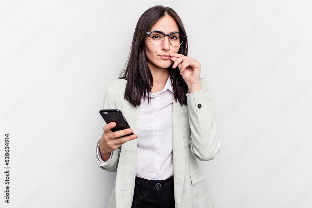Young business caucasian woman holding mobile phone isolated on white background with fingers on lips keeping a secret. Young business caucasian woman holding mobile phone isolated on white background with fingers on lips keeping a secret.