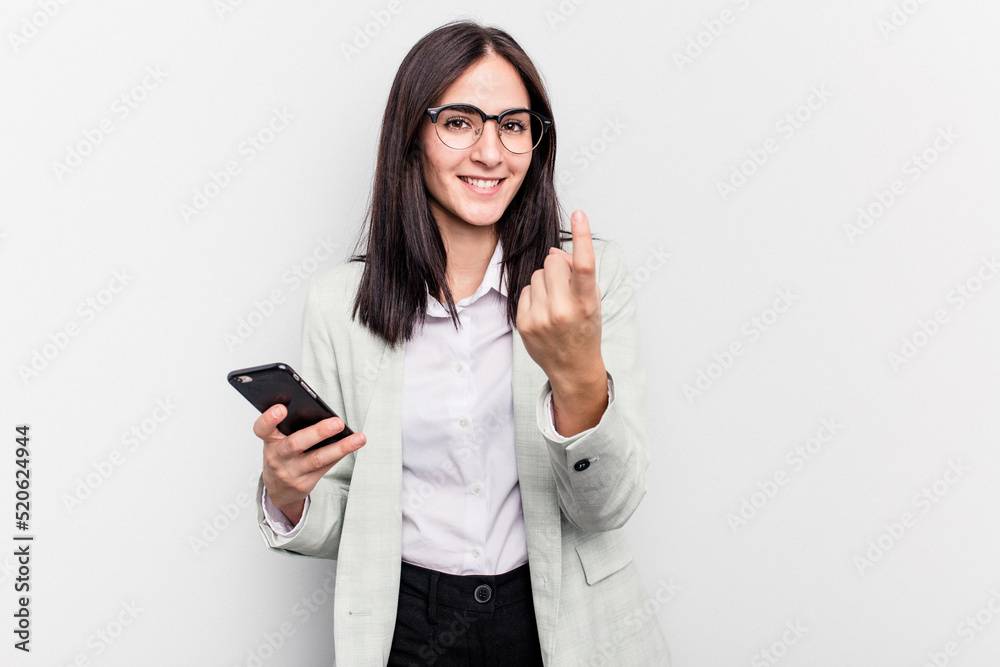 Young business caucasian woman holding mobile phone isolated on white background pointing with finger at you as if inviting come closer. Young business caucasian woman holding mobile phone isolated on white background pointing with finger at you as if inviting come closer.