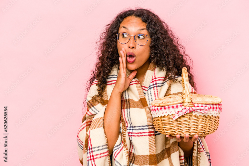Young hispanic woman doing a picnic isolated on beige background is saying a secret hot braking news and looking aside