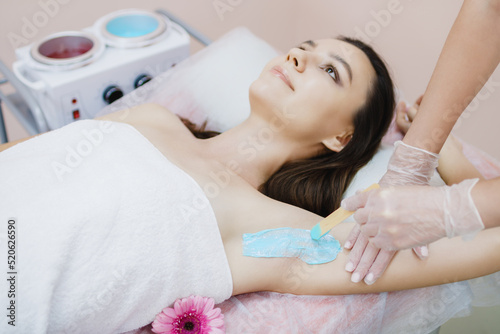 A master applies depilatory wax to the armpit of a young beautiful woman to remove unwanted hair. Sugaring. Depilation. Epilation. Beauty Concept. Selective focus on a girl's armpit with wax applied.