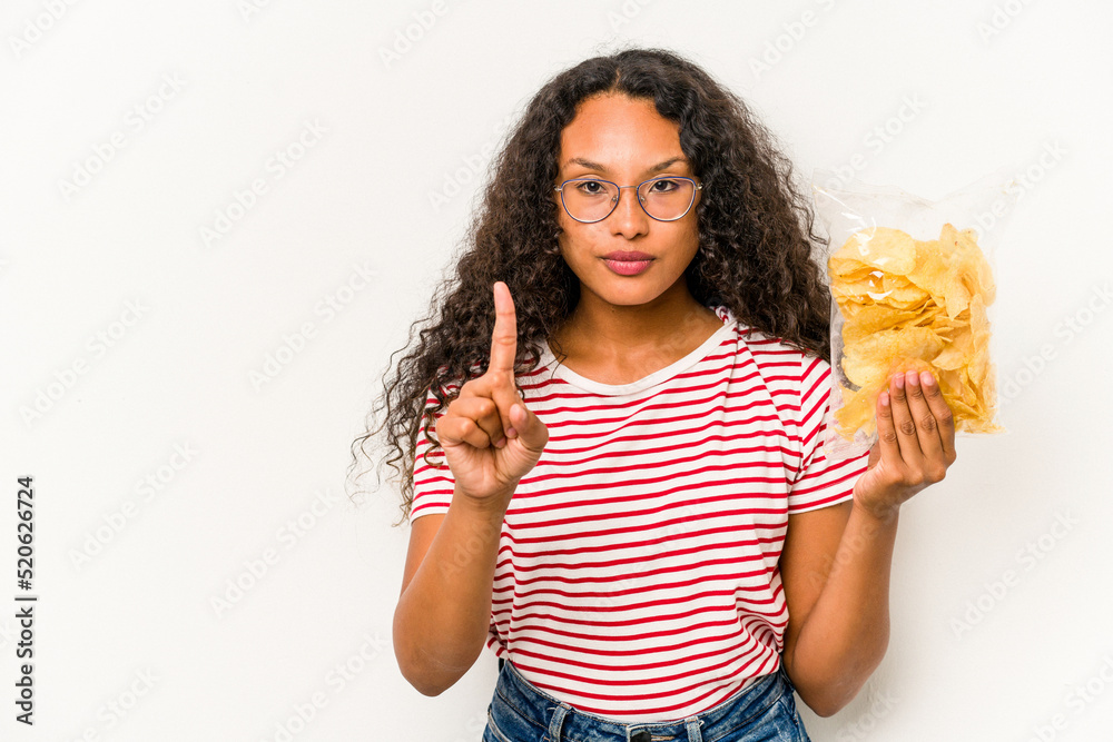 Young hispanic woman holding crips isolated on white background showing number one with finger.