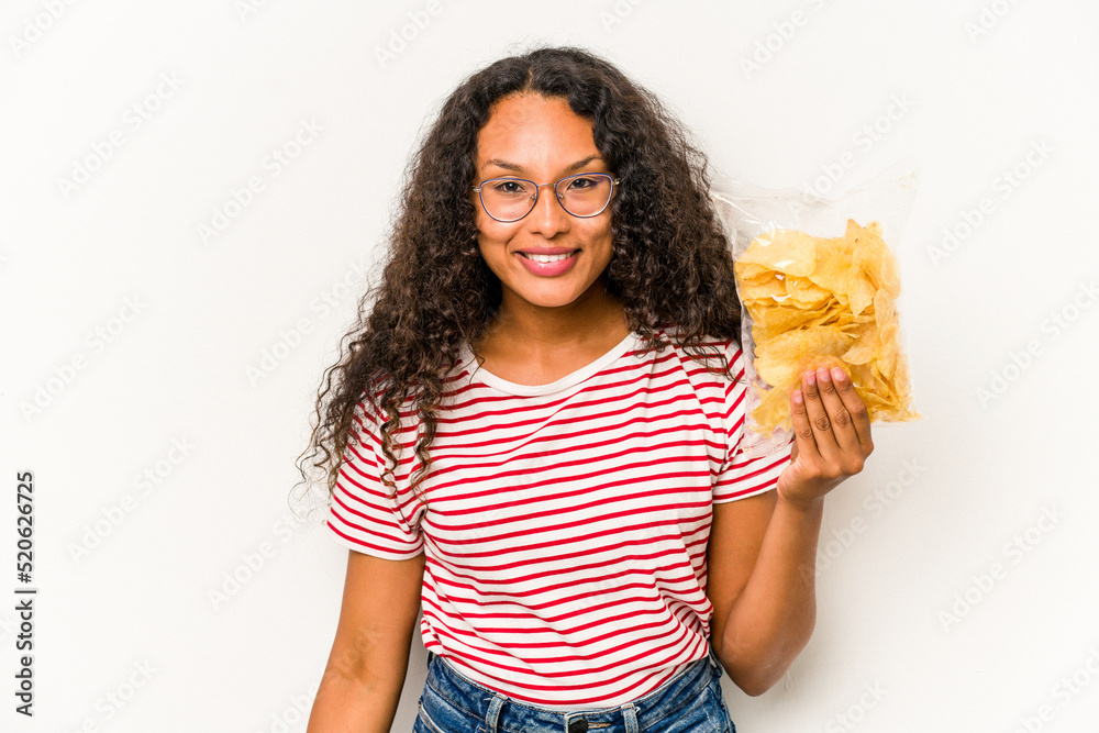 Young hispanic woman holding crips isolated on white background happy, smiling and cheerful. Young hispanic woman holding crips isolated on white background happy, smiling and cheerful.